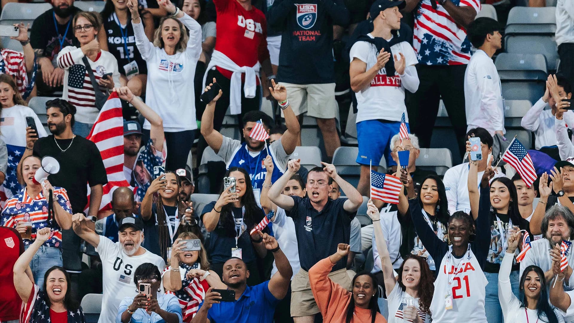 TEAM USA FOOTBALL® fans waving American flags and cheering in stadium bleachers at an international competition.